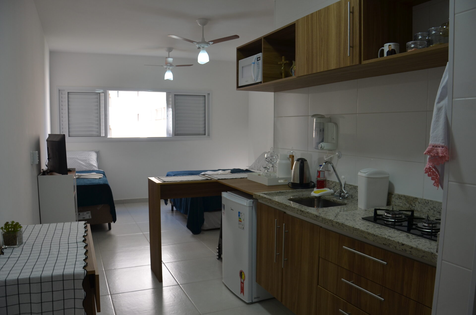 Visão geral da kitnet do Apartamento 313, com cama de casal e cozinha equipada — Kadosch Empreendimentos, Cachoeira Paulista/SP, perto da Canção Nova