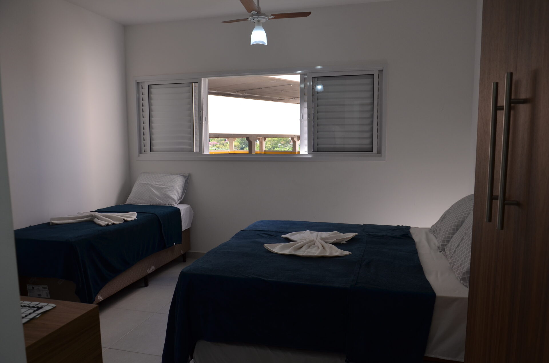 Quarto do Apartamento 313 com cama de casal, cama de solteiro e janela — Kadosch Empreendimentos, Cachoeira Paulista/SP, perto da Canção Nova